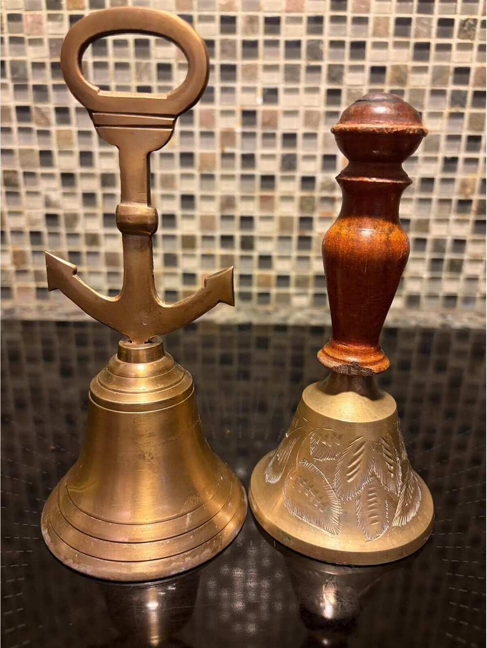 A pair of vintage brass handbells featuring a wooden handle and an anchor design